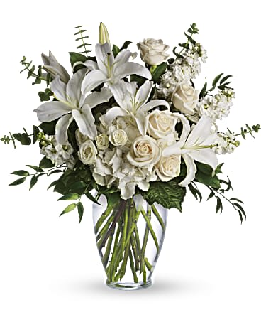 Tall arrangement of white lilies, roses, and other white flowers in a clear glass vase