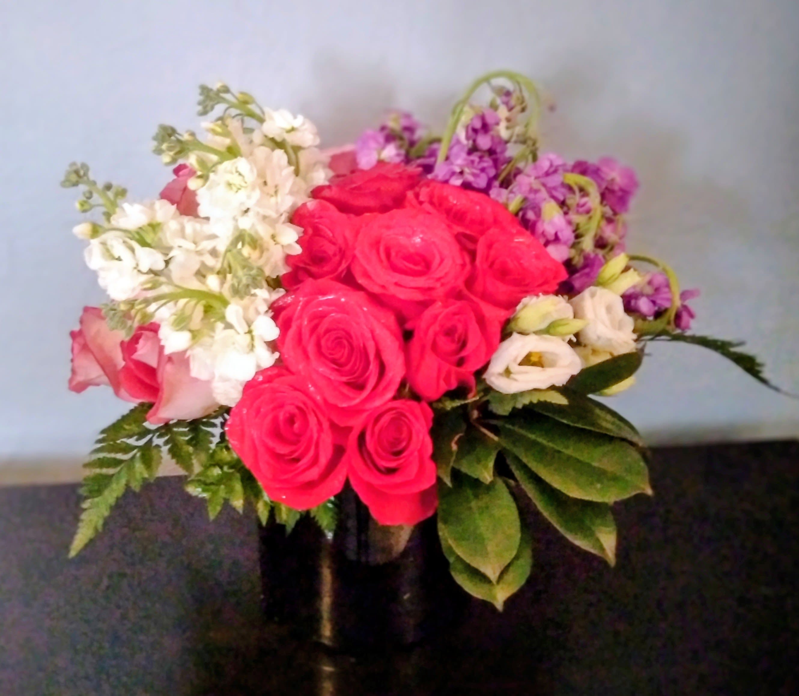 Bouquet of pink roses, white blooms, and purple flowers in a dark vase