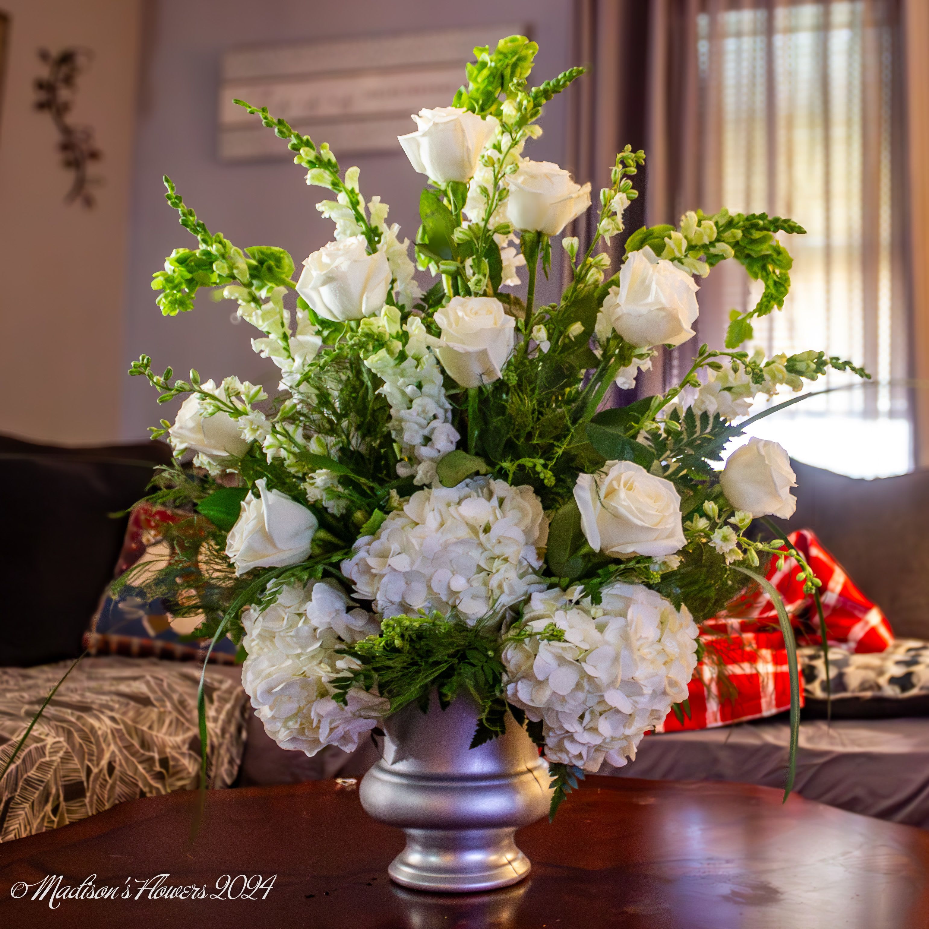 Classic Sympathy in white and silver by Madison's Flowers - A classic Sympathy arrangement of white hydrangea, white roses, white snapdragons, white larkspur, and bright green bells or Ireland. Thoughtfully arranged in a silver urn. 