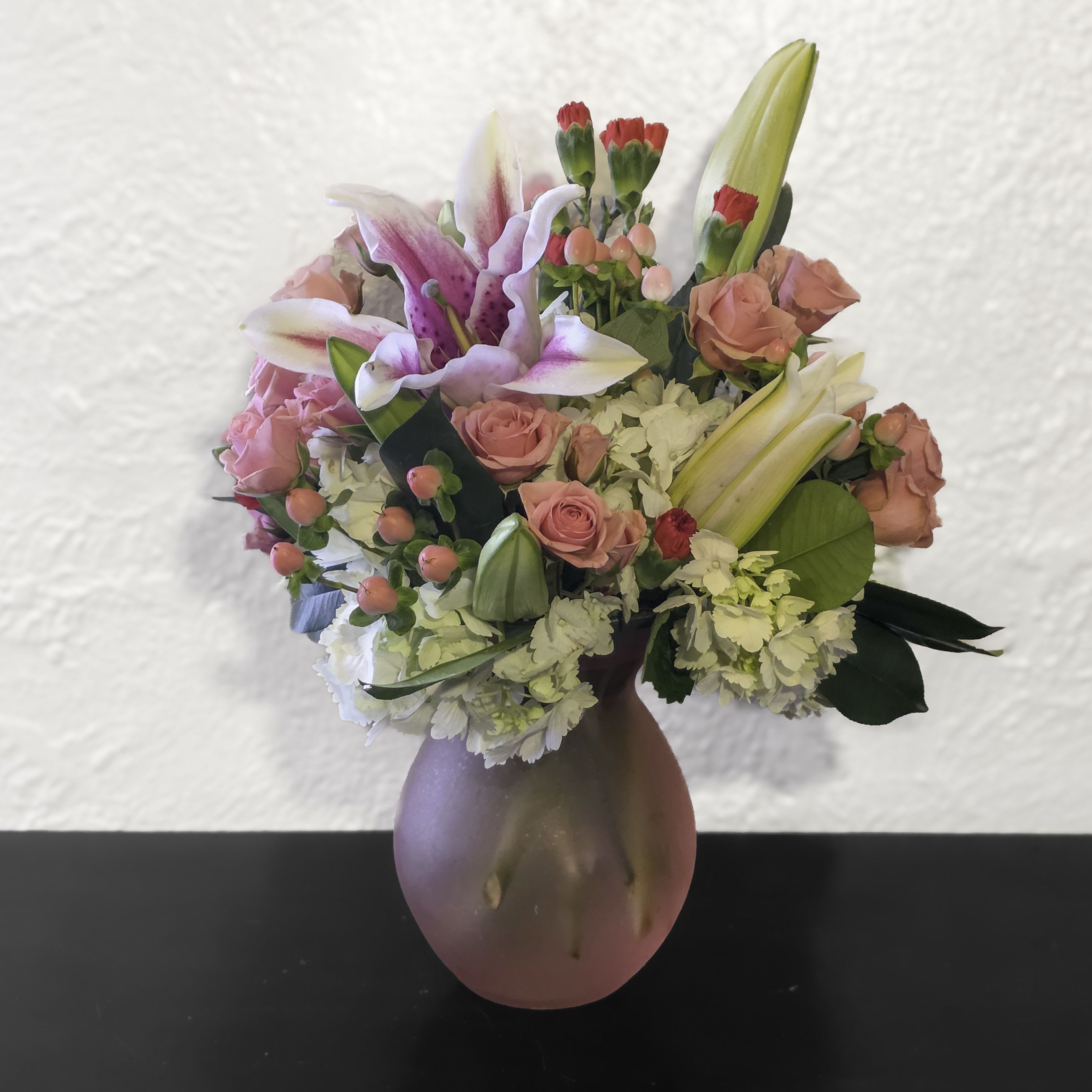 Pink and white lilies, roses, and carnations arranged in a frosted pink glass vase.