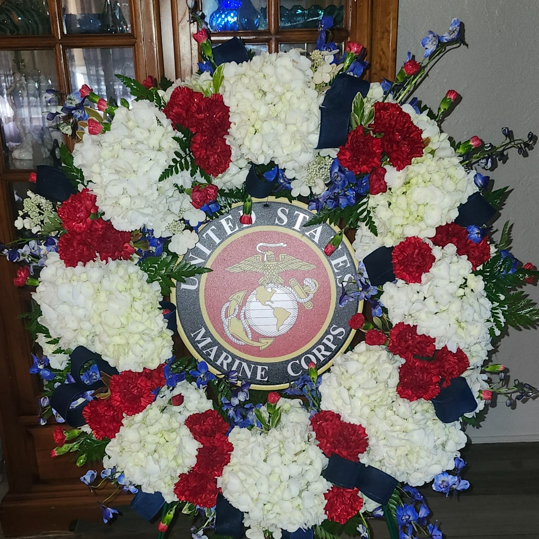 Large floral wreath with red, white, and blue flowers around a Marine Corps emblem