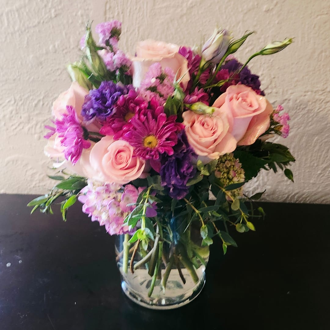 Pink roses and purple mixed flowers arranged in a clear glass vase.