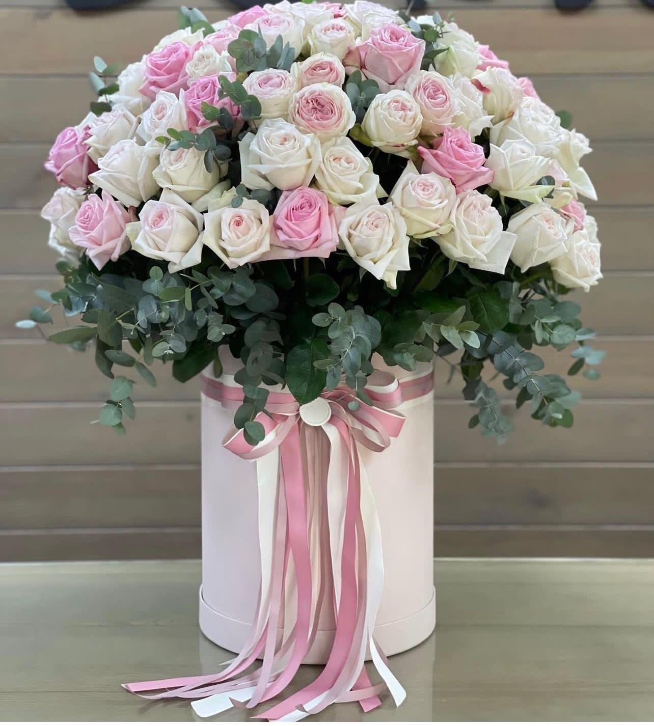Pink and white roses in a round hatbox with ribbon streamers