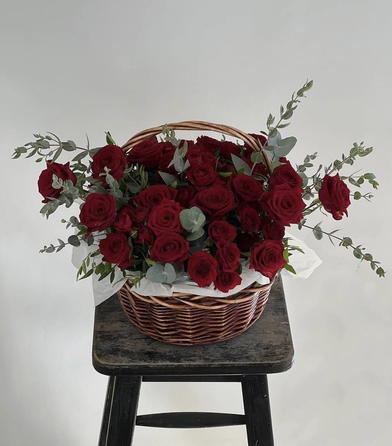 Basket of red roses with eucalyptus on a stool