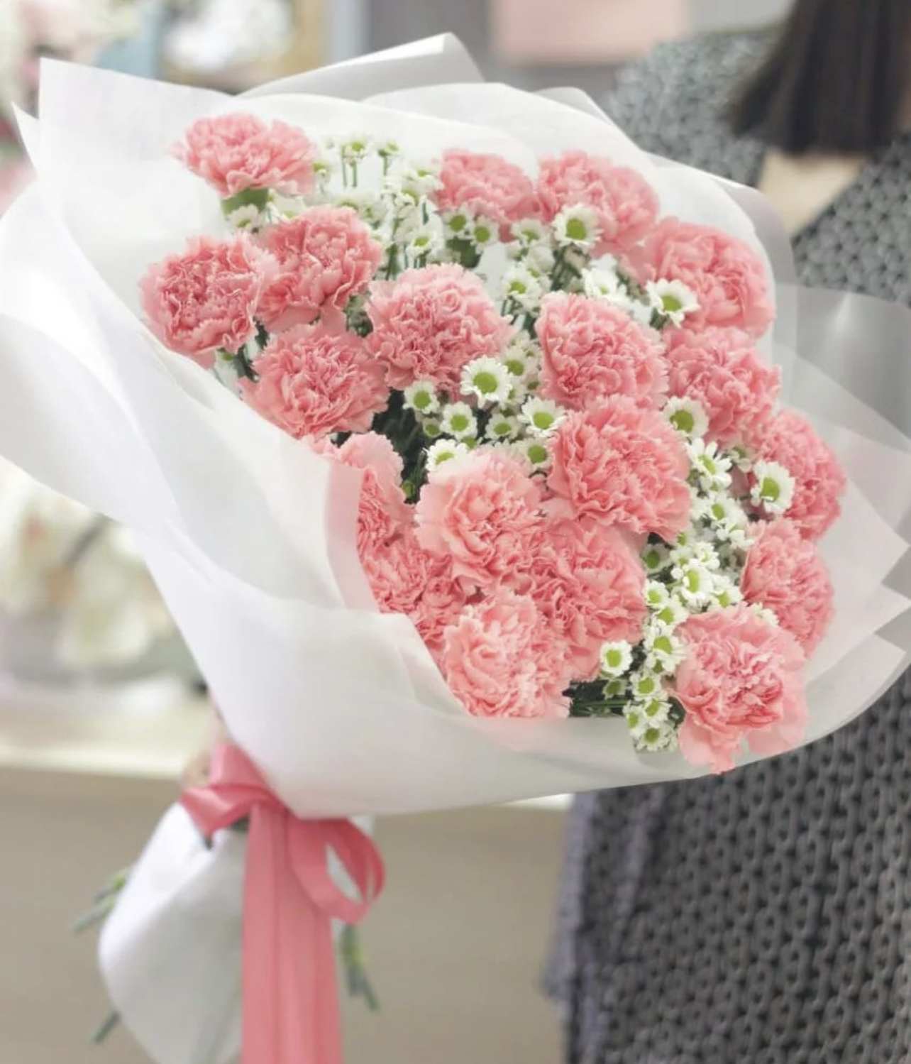Pink carnations and small white daisies wrapped in white paper with a pink ribbon