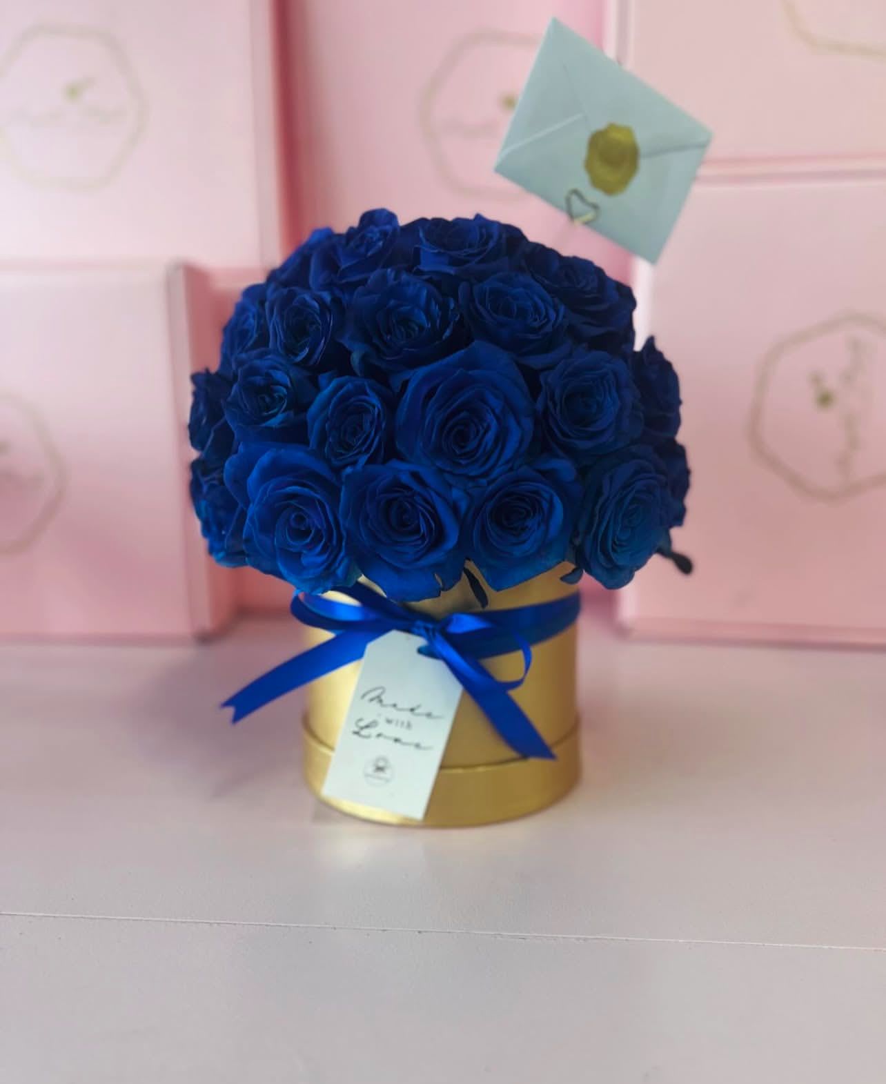 Blue roses arranged in a gold hatbox with a ribbon