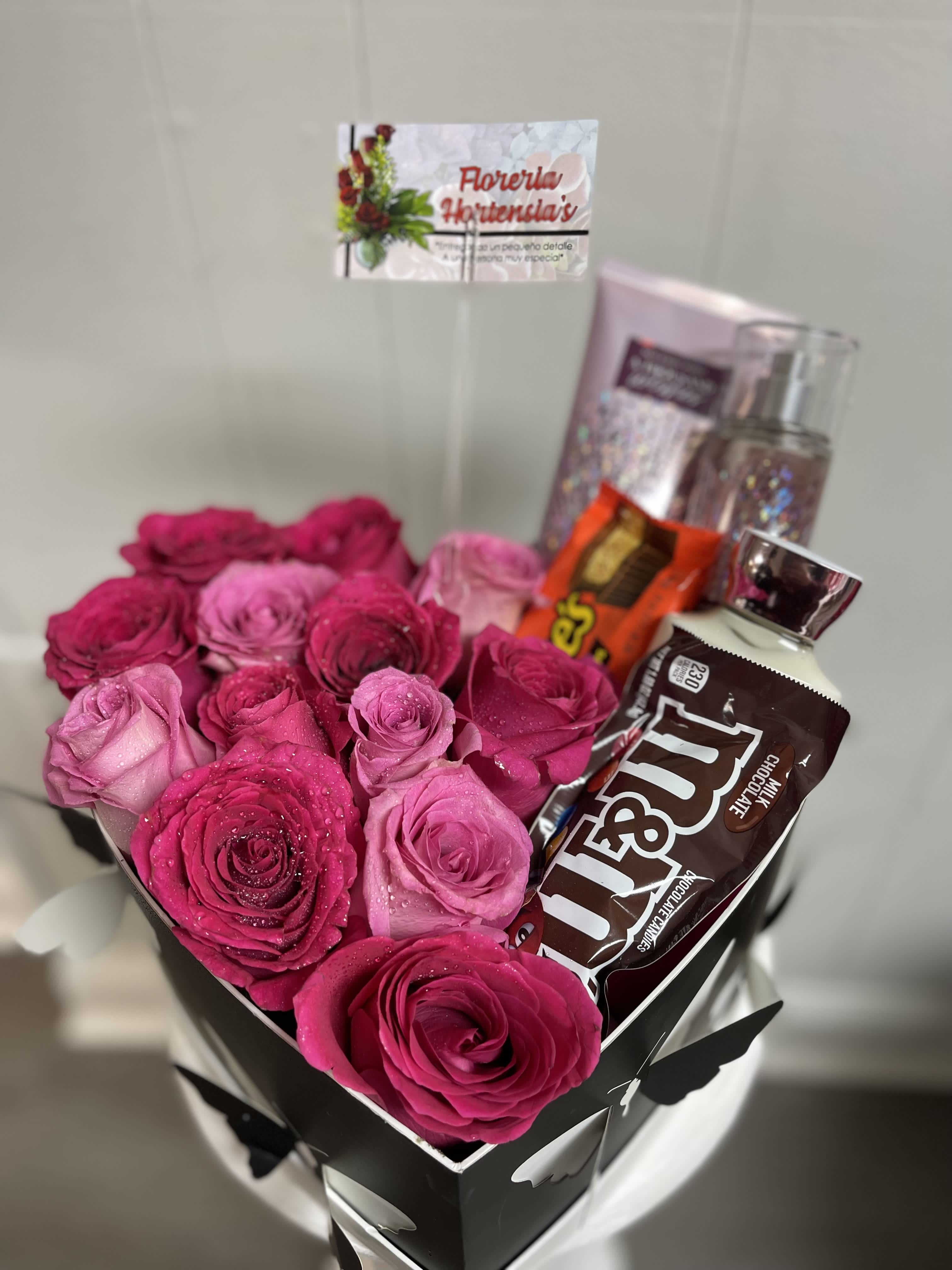 Pink and magenta roses in a black gift box with chocolates and perfume