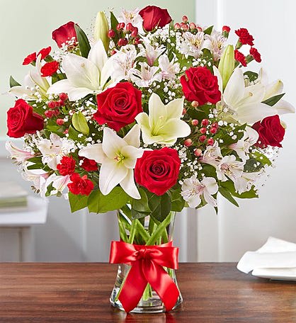 Bouquet of red roses and white lilies in a glass vase with a red ribbon