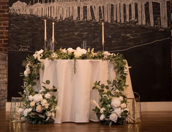 Purity of Love Sweetheart Table (Wedding) - white roses, baby breath, white Lilies and greenery.  This order come with one garland and two floor displays corner of the table from our Purity of love wedding package. We can also custom toyour wedding theme color.