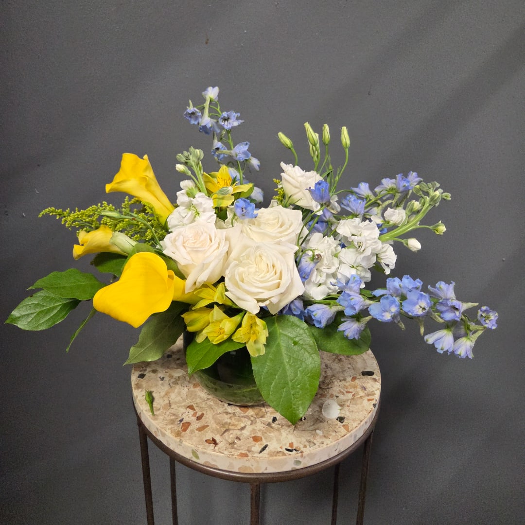 Yellow calla lilies, white roses, and blue flowers in a low vase