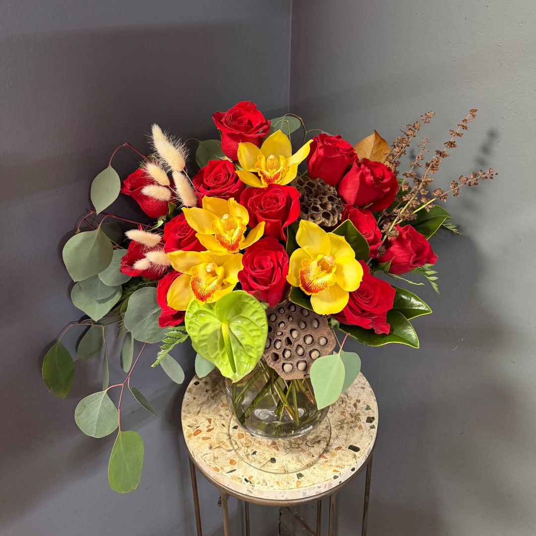Red roses and yellow orchids arranged in a glass vase