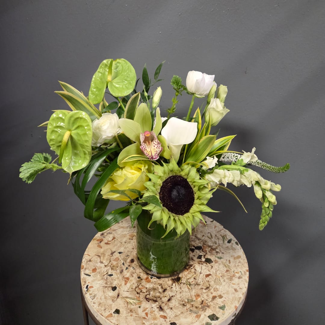 Mixed floral arrangement in a green glass vase with white and green blooms
