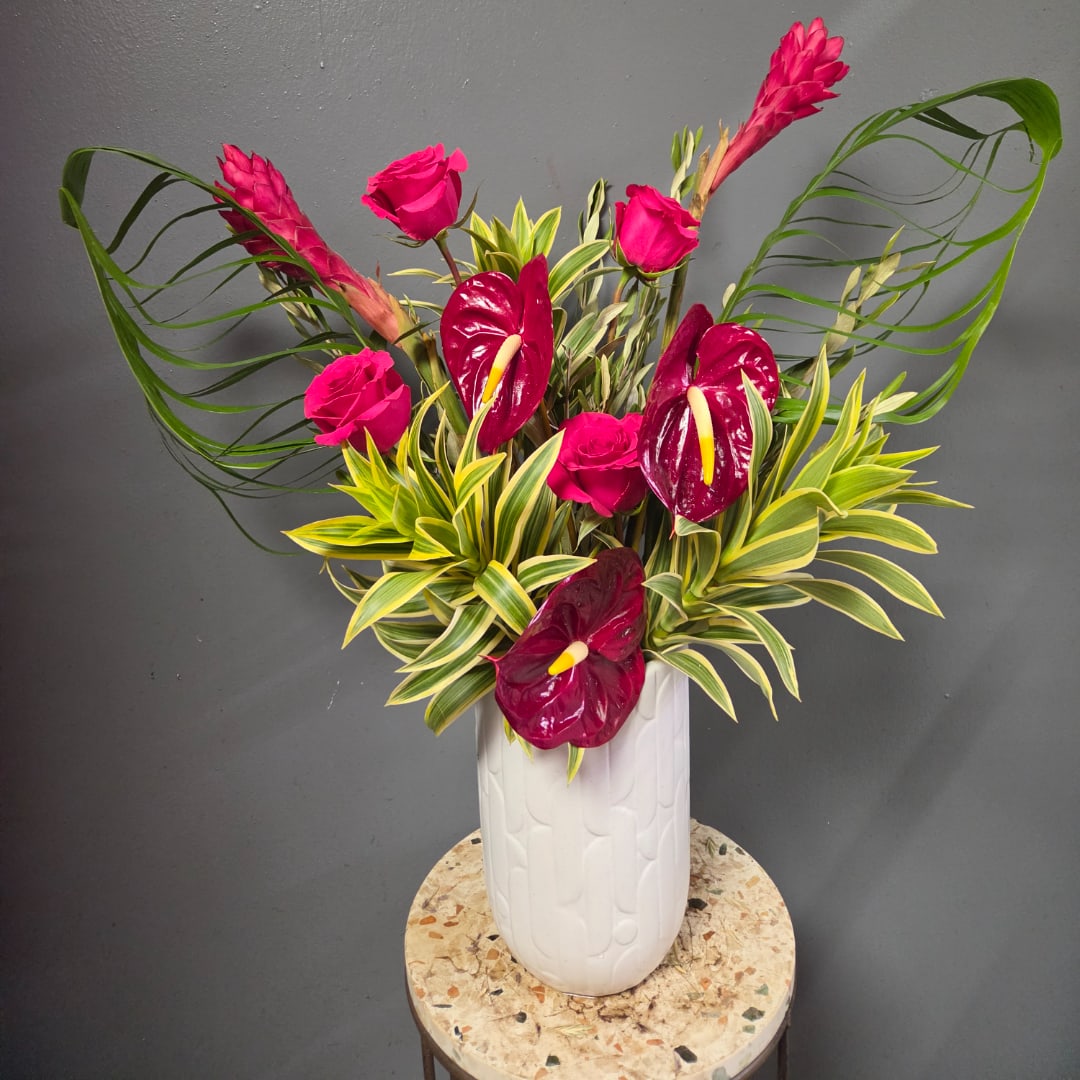 Pink roses and burgundy anthuriums in a white vase with variegated foliage