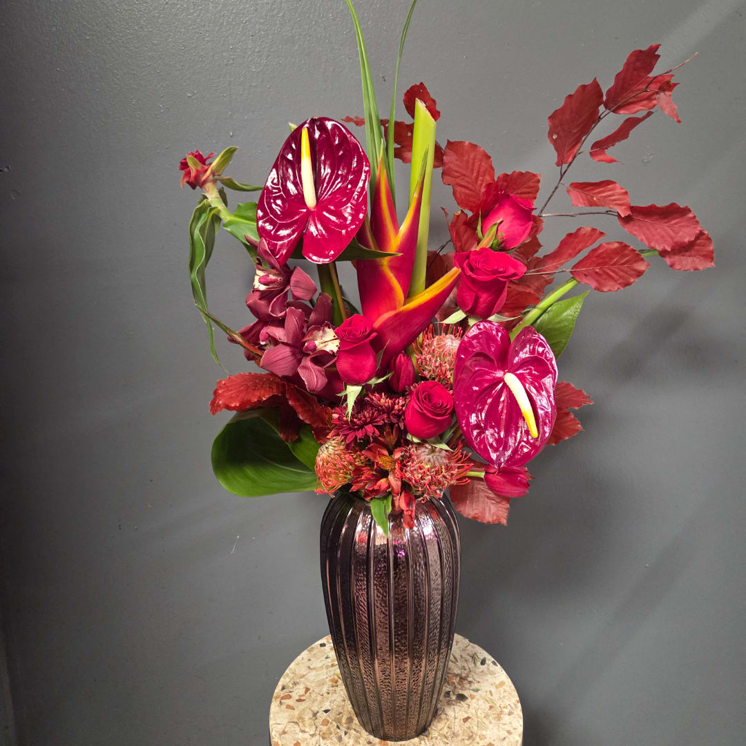 Tall tropical bouquet in a dark ribbed vase with red and pink blooms