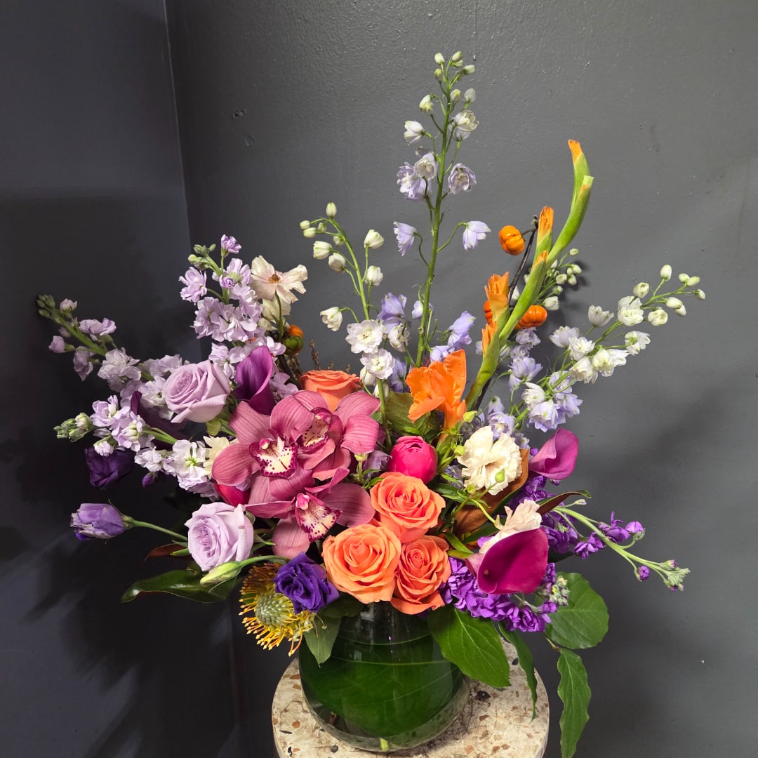Colorful mixed bouquet in a green glass vase with roses, orchids, and purple blooms