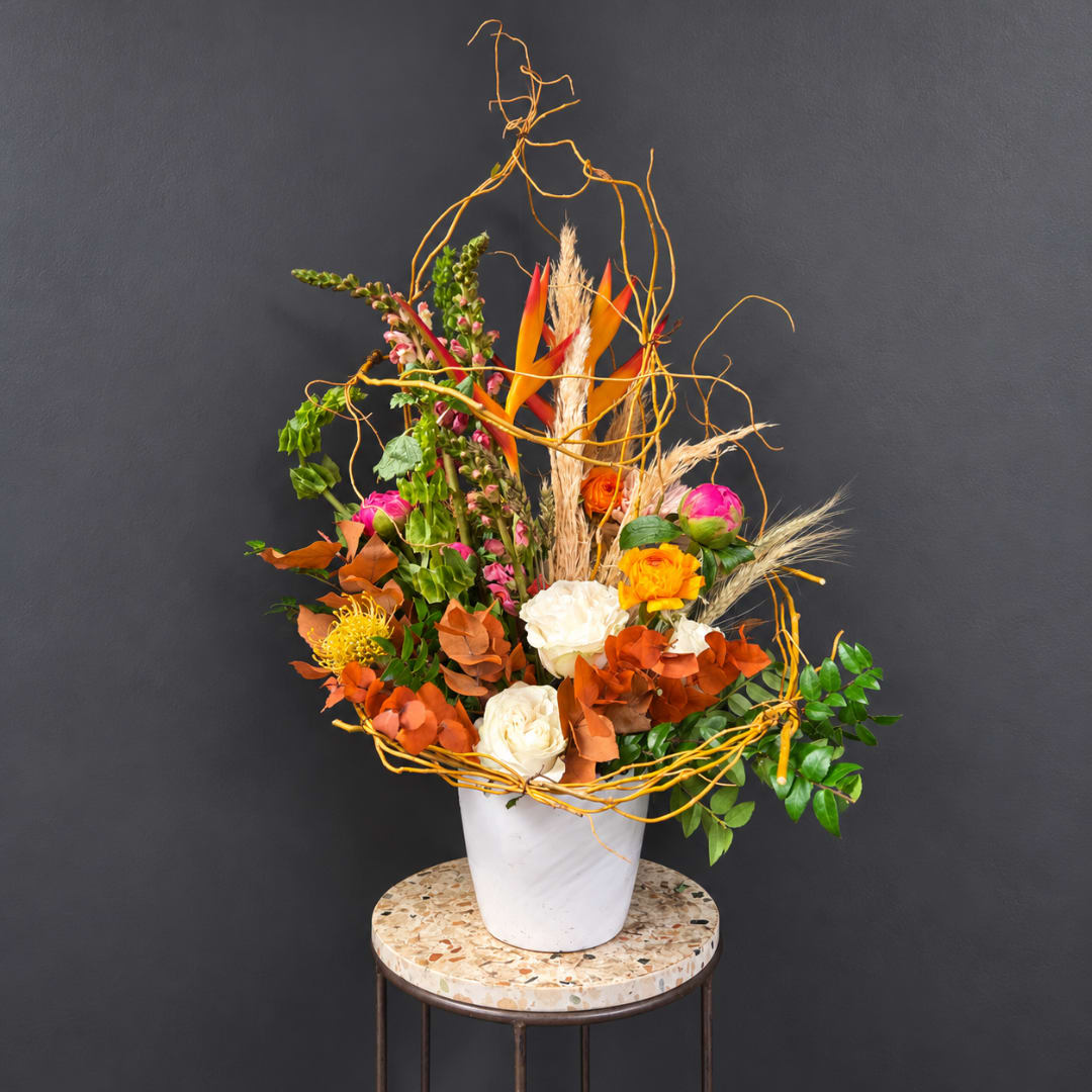 Tall floral arrangement with orange, pink, and white blooms in a white vase