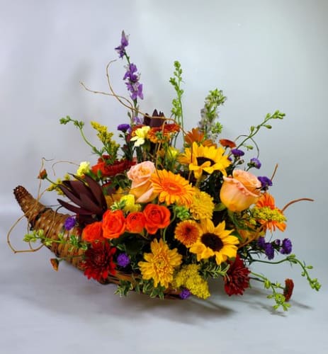 Mixed bouquet in a woven basket with sunflowers, roses, and orange blooms