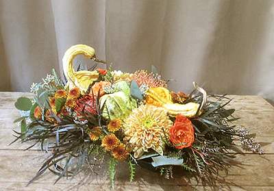 Low autumn centerpiece with gourd swans and orange and yellow flowers in an oval arrangement