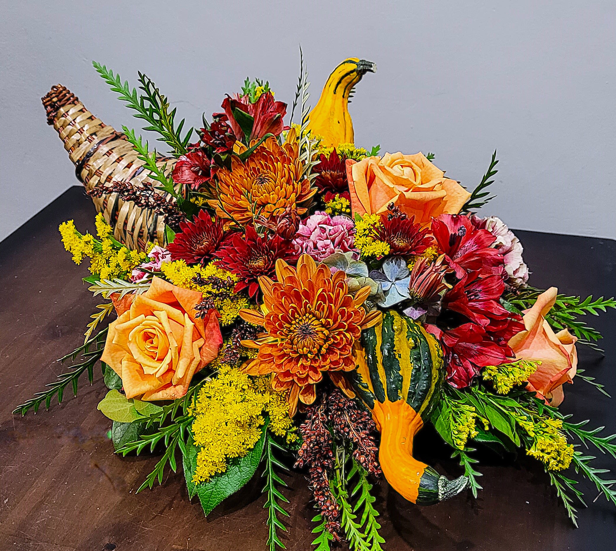 Autumn centerpiece with orange roses, mums, red flowers and gourds in a woven cornucopia