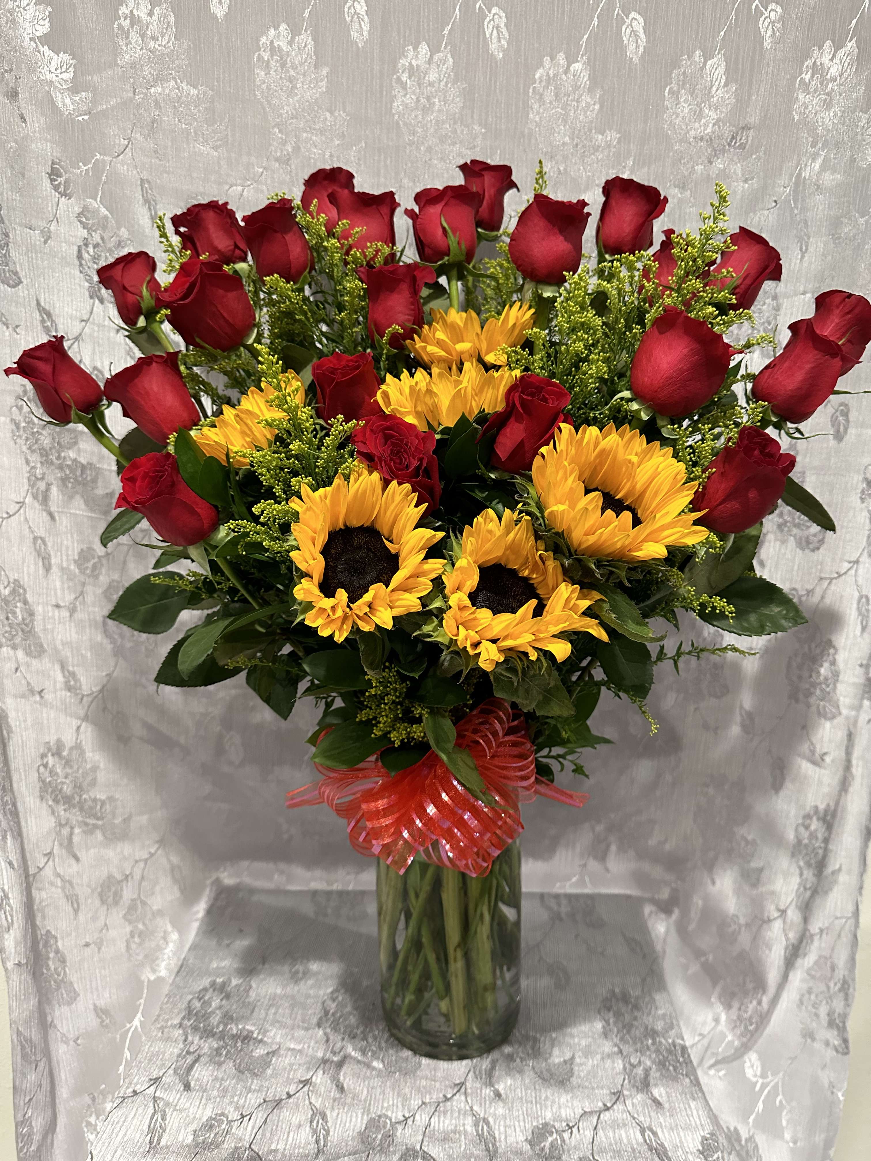 Red roses and yellow sunflowers in a glass vase with a red ribbon