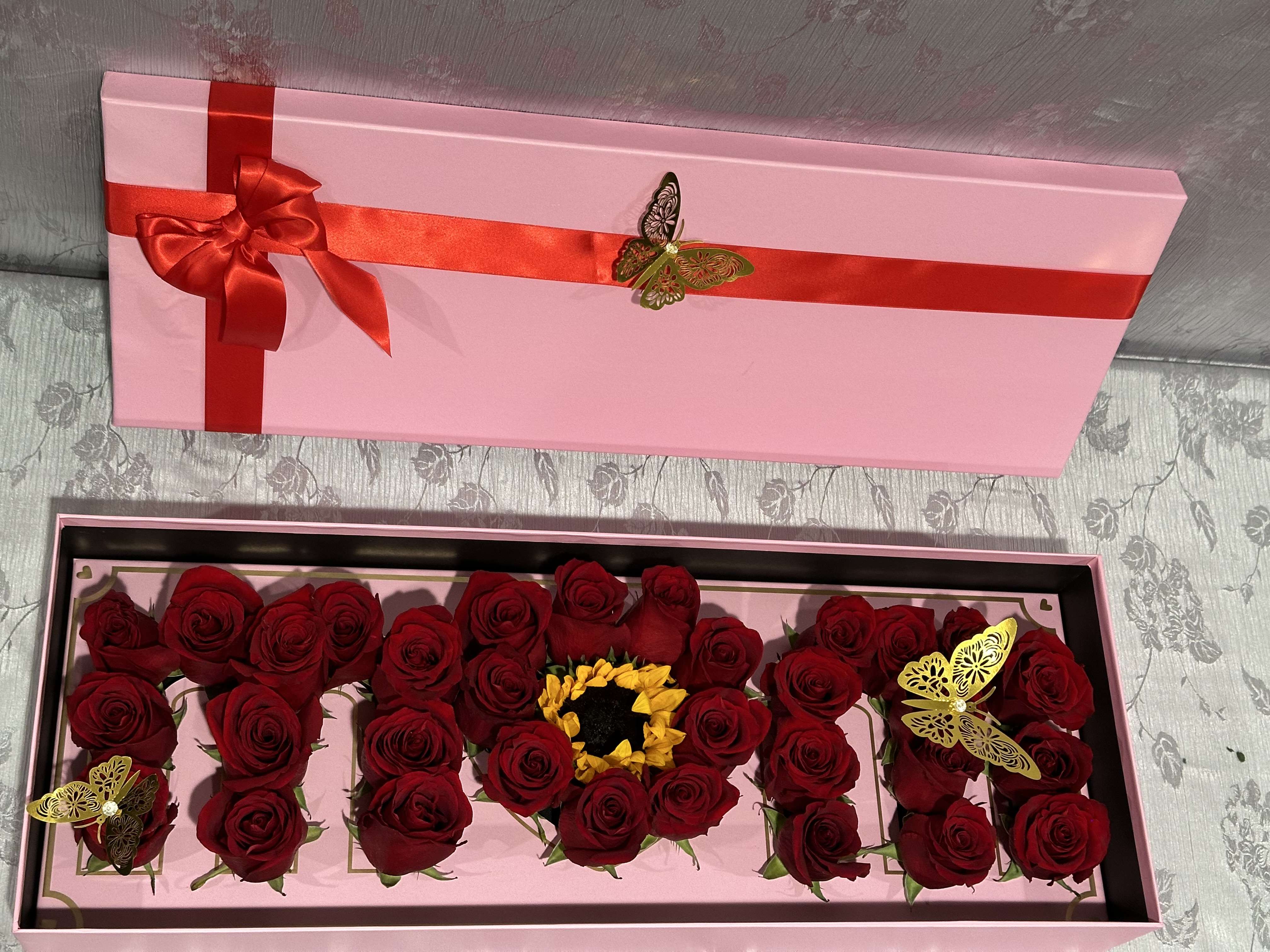 Pink gift box with red roses arranged inside and a red ribbon on the lid