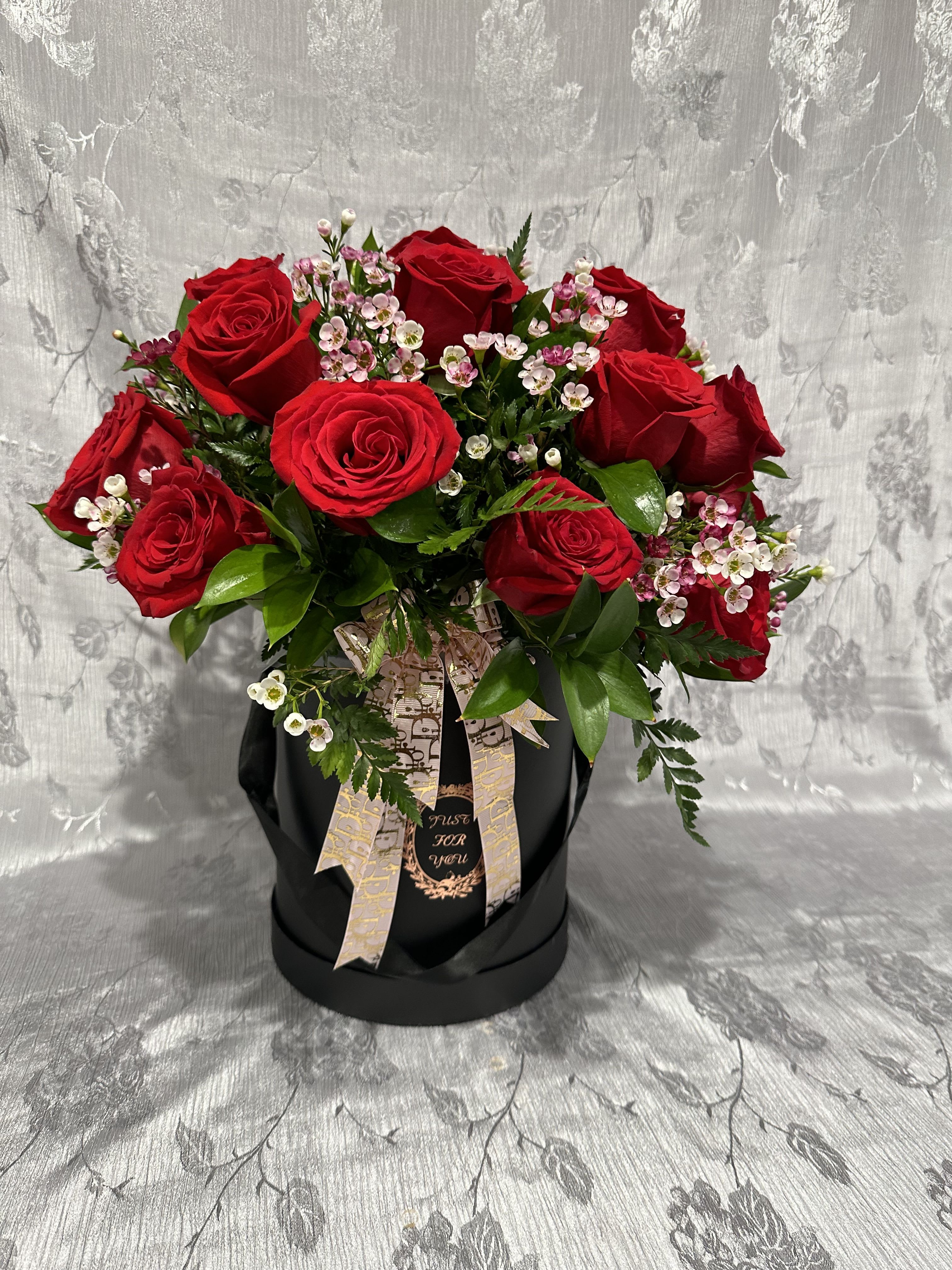Red roses arranged in a black hatbox with pink filler flowers.