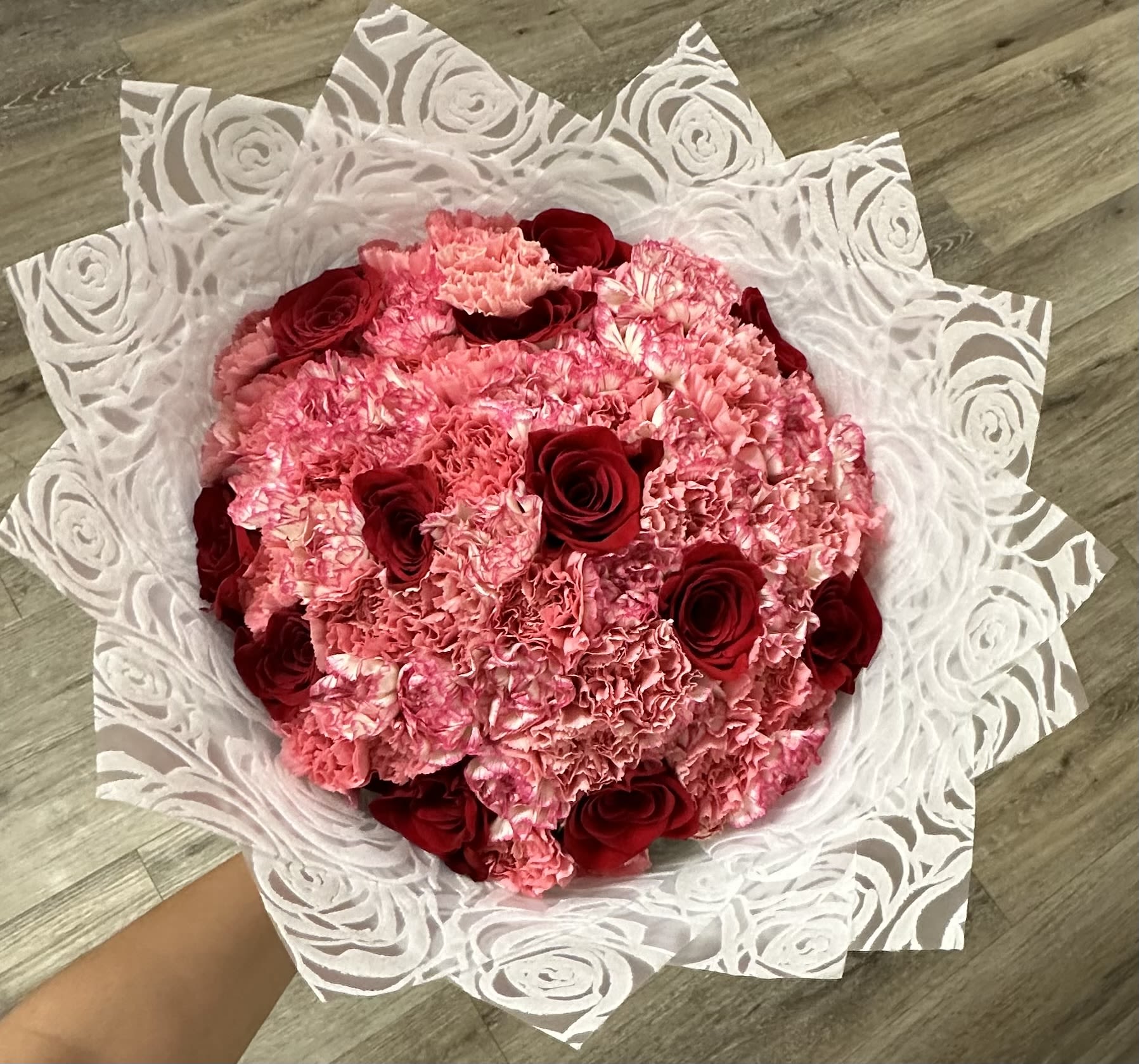 Pink carnation bouquet with red roses wrapped in white patterned paper