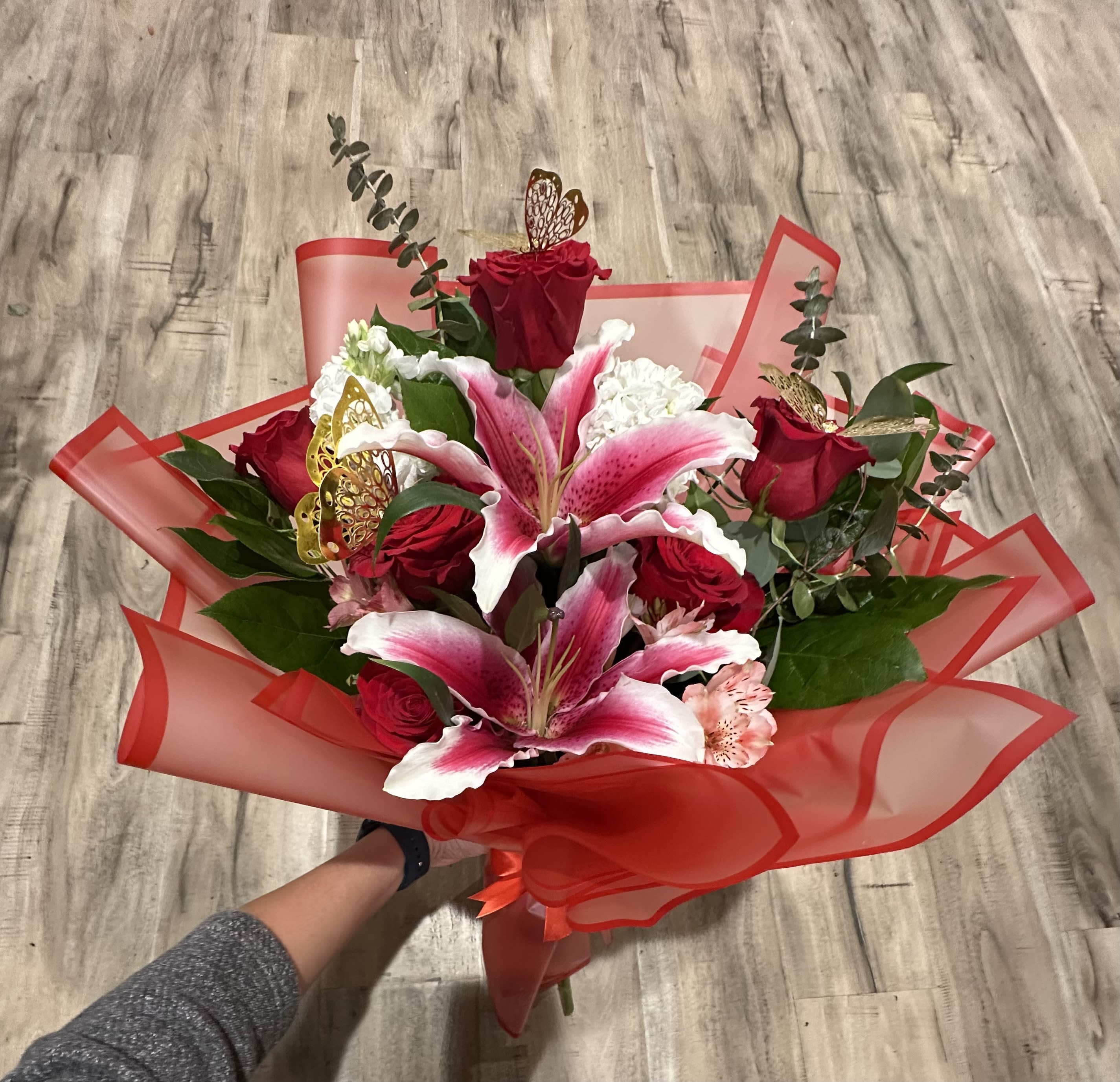 Handheld bouquet of red roses and pink lilies wrapped in red paper