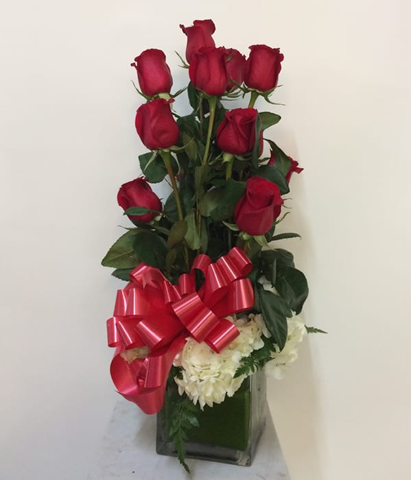 Tall arrangement of red roses with white flowers in a glass vase and red bow