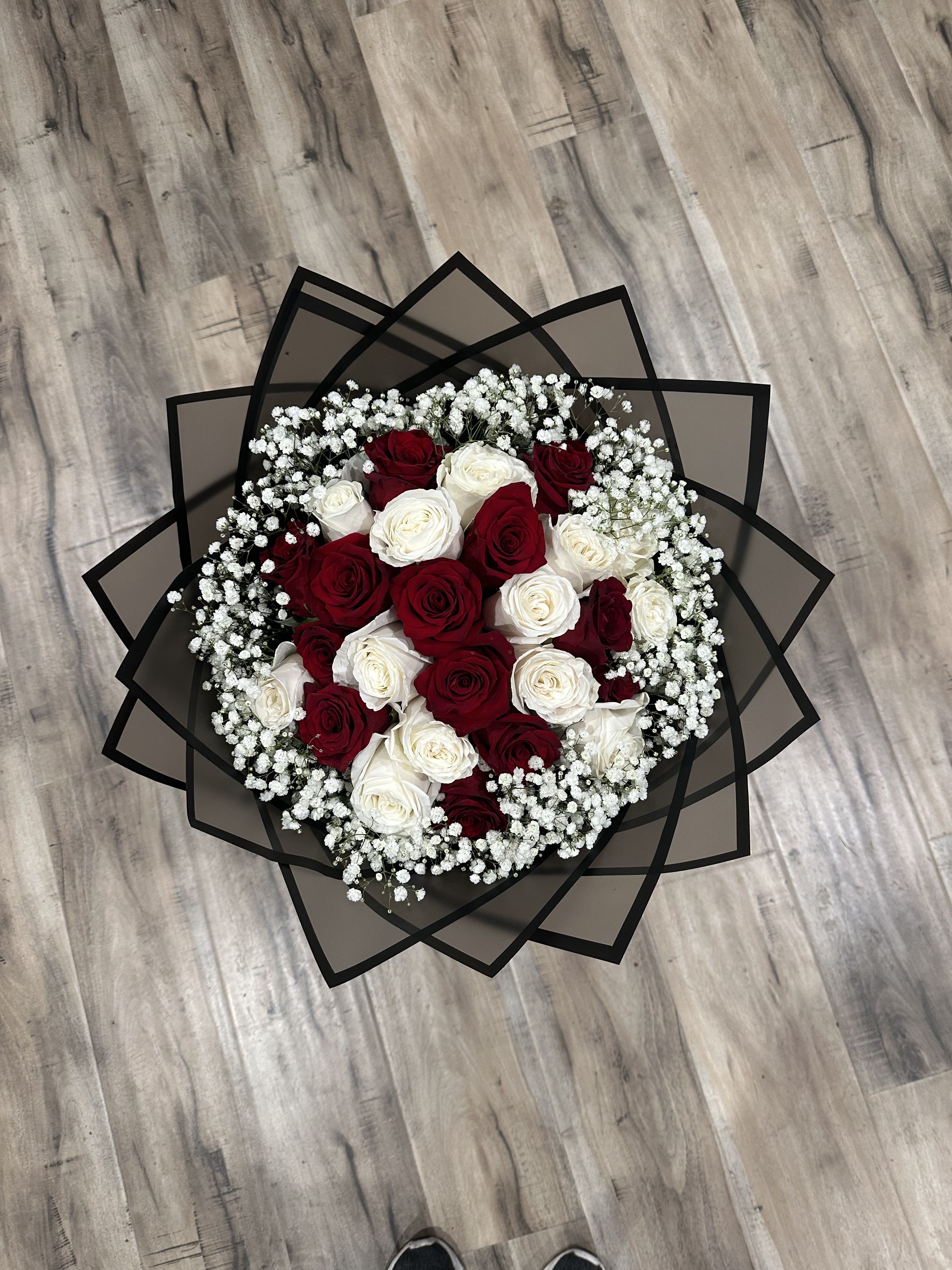 Round bouquet of red and white roses with baby's breath in black wrap