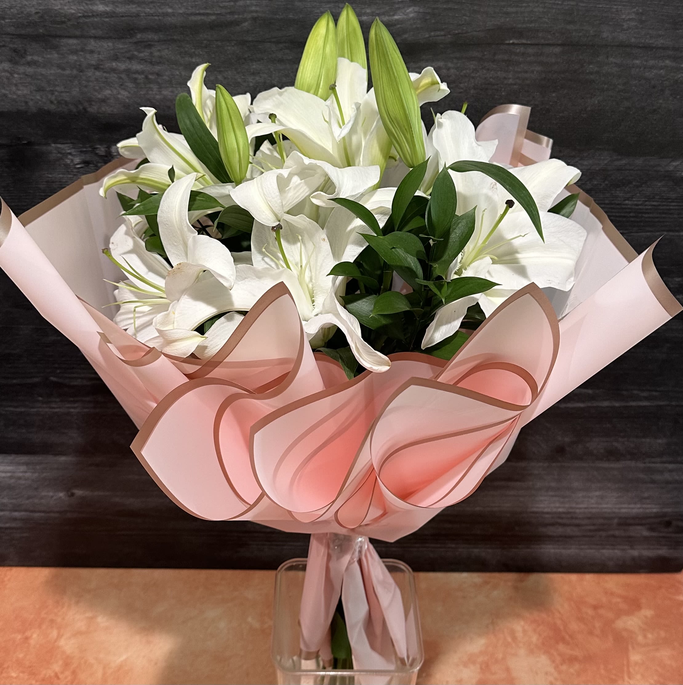 White lilies in pink wrapping with a clear vase