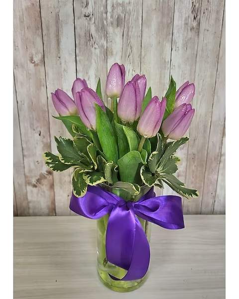 Pink tulips in a clear glass vase with a purple ribbon