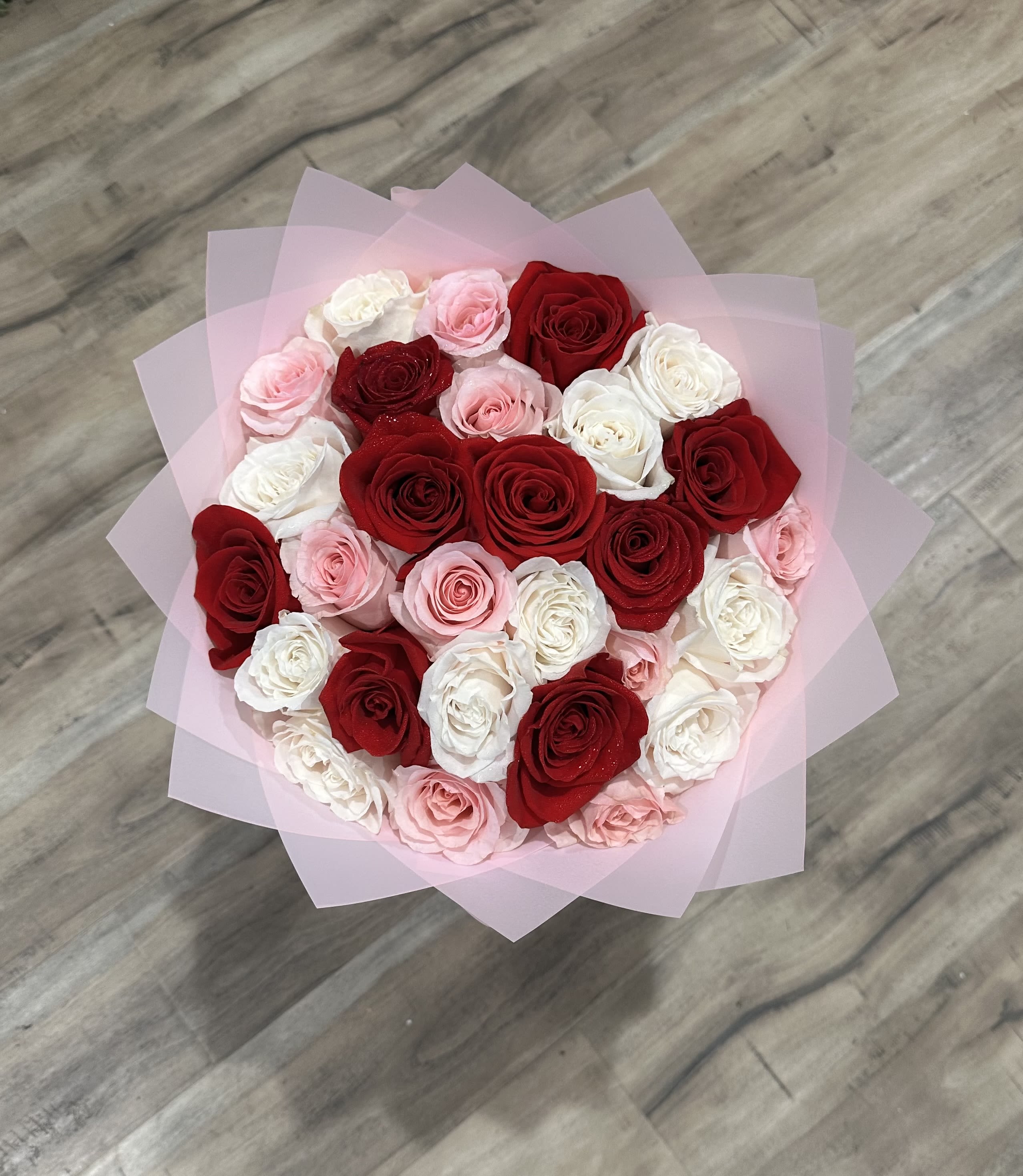 Bouquet of red, pink, and white roses wrapped in pale pink paper