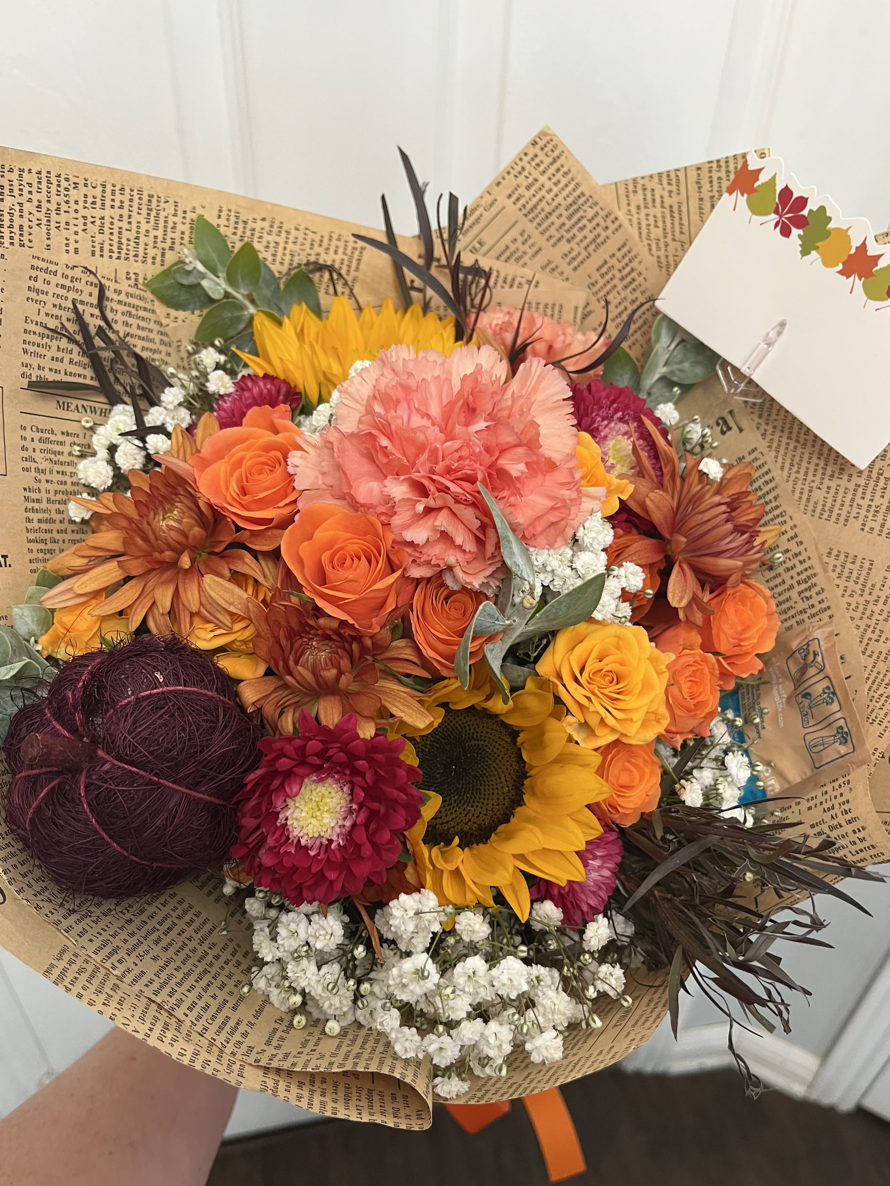 Mixed bouquet with orange roses, sunflowers, and pink carnations in brown paper