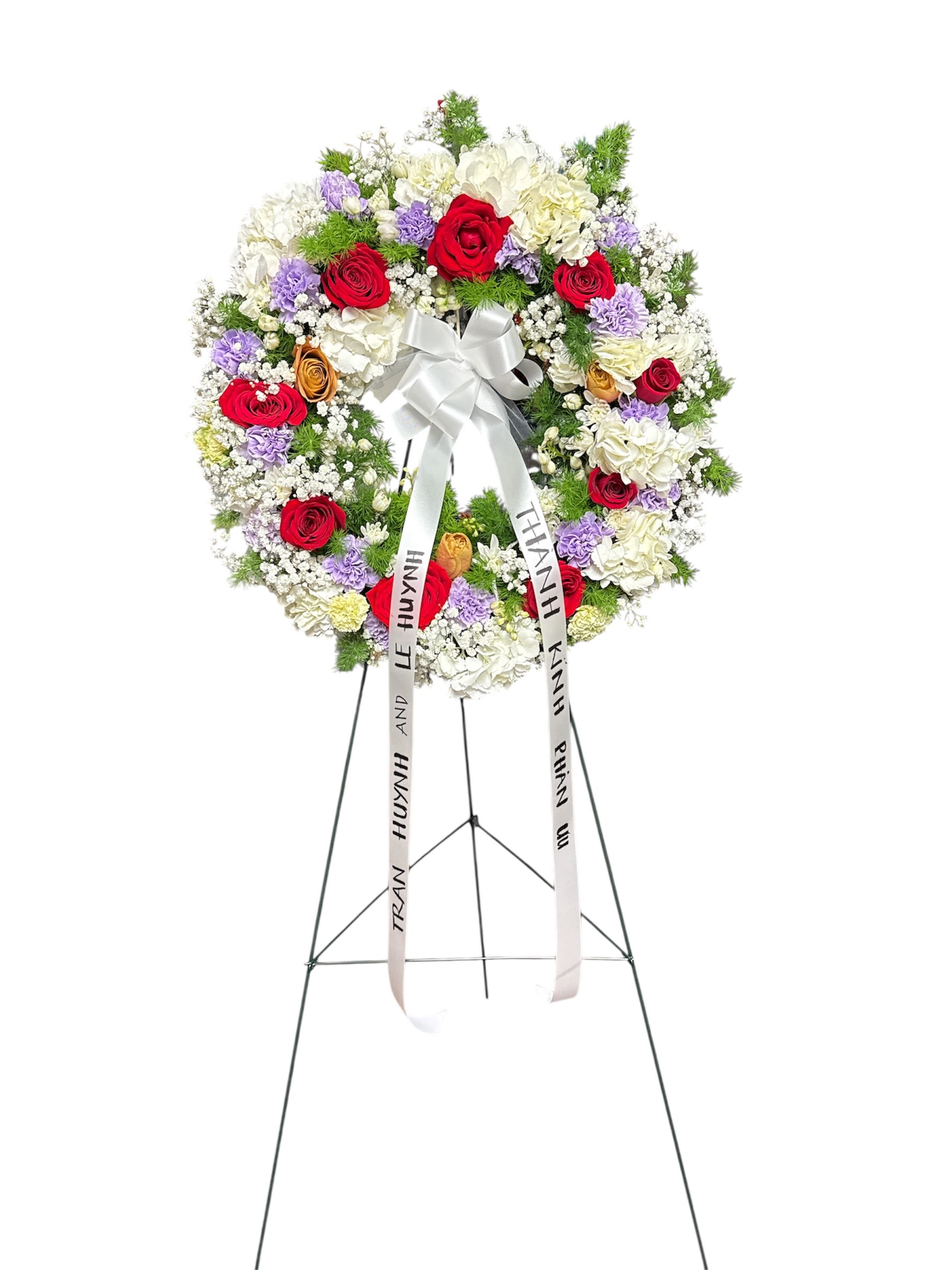 Circular funeral wreath of red, white, and lavender flowers on a stand
