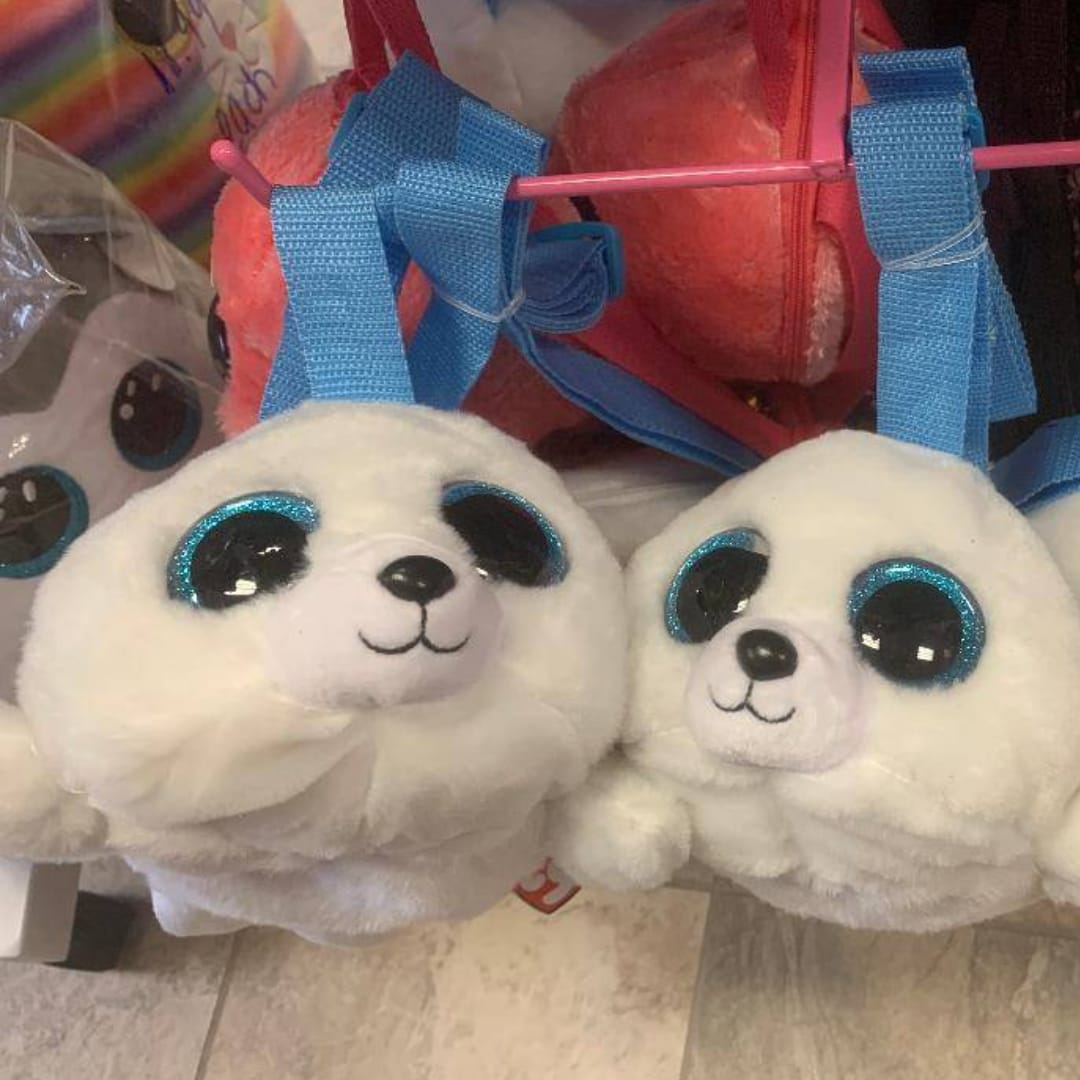 Two white plush seal toys with glittery blue eyes sit in a gift display.