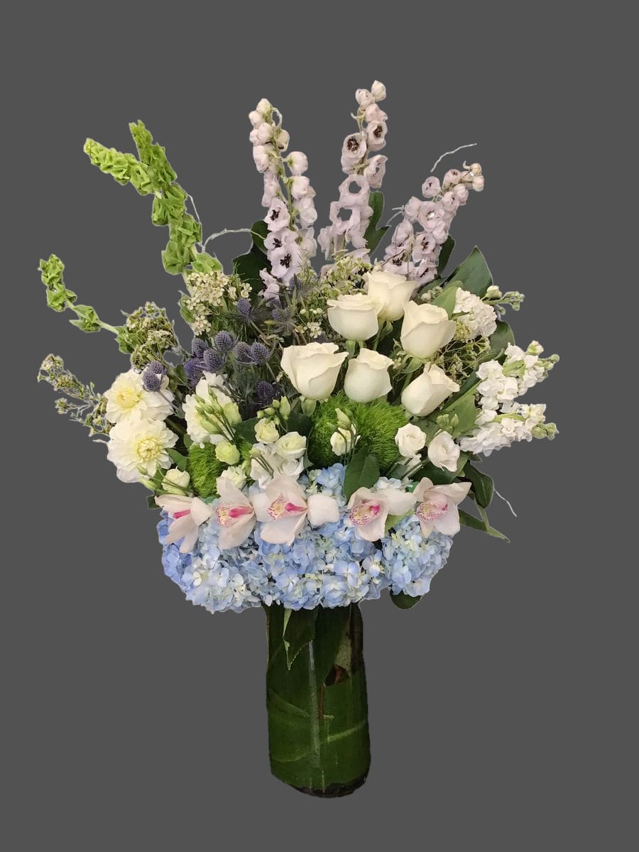 Tall bouquet of white roses, blue hydrangeas, and pale orchids in a glass vase