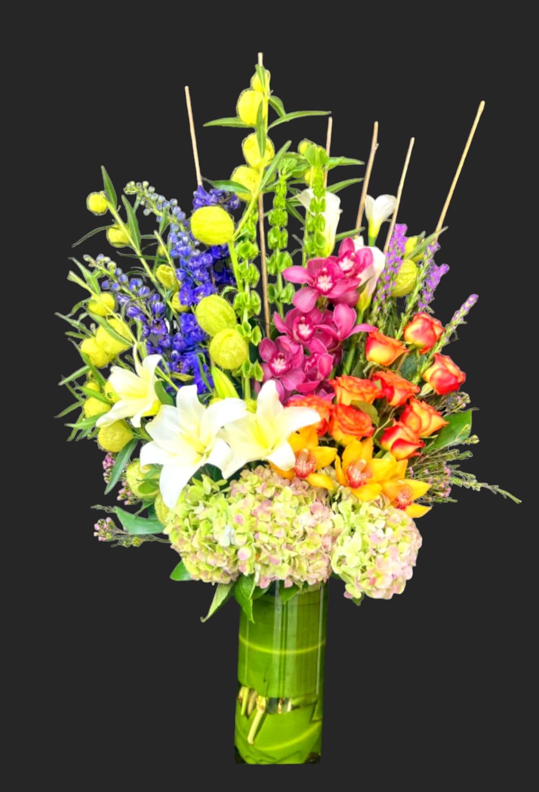 Tall mixed bouquet in a green vase with white lilies and bright orchids