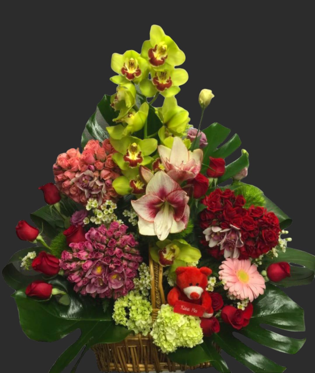 Mixed flower basket with orchids, roses, hydrangeas, and a small teddy bear
