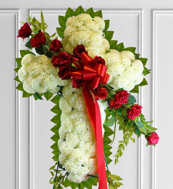 Cross-shaped floral spray with white blooms, red roses, and a red ribbon