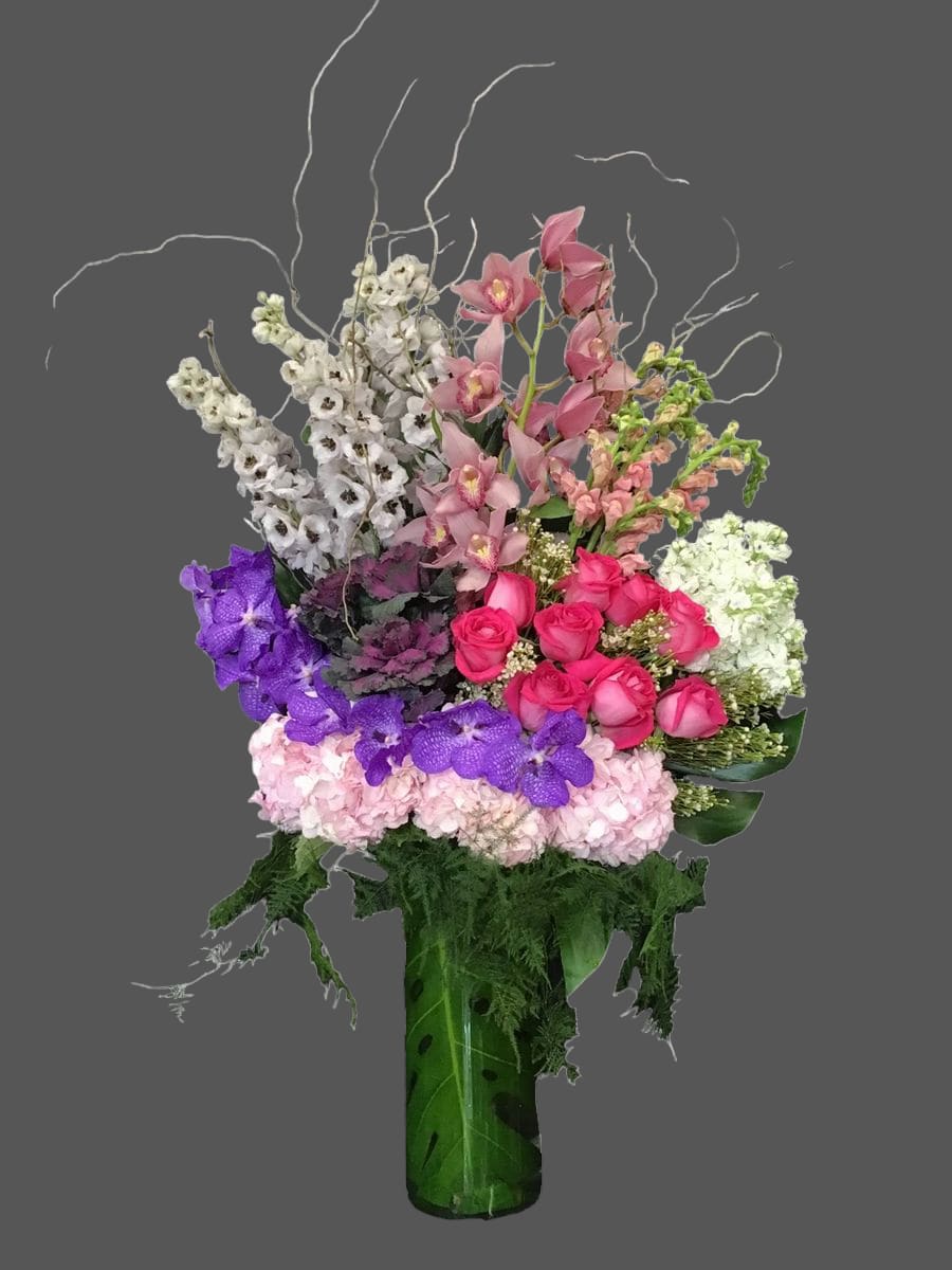 Tall mixed bouquet with pink roses, orchids, and purple flowers in a green vase