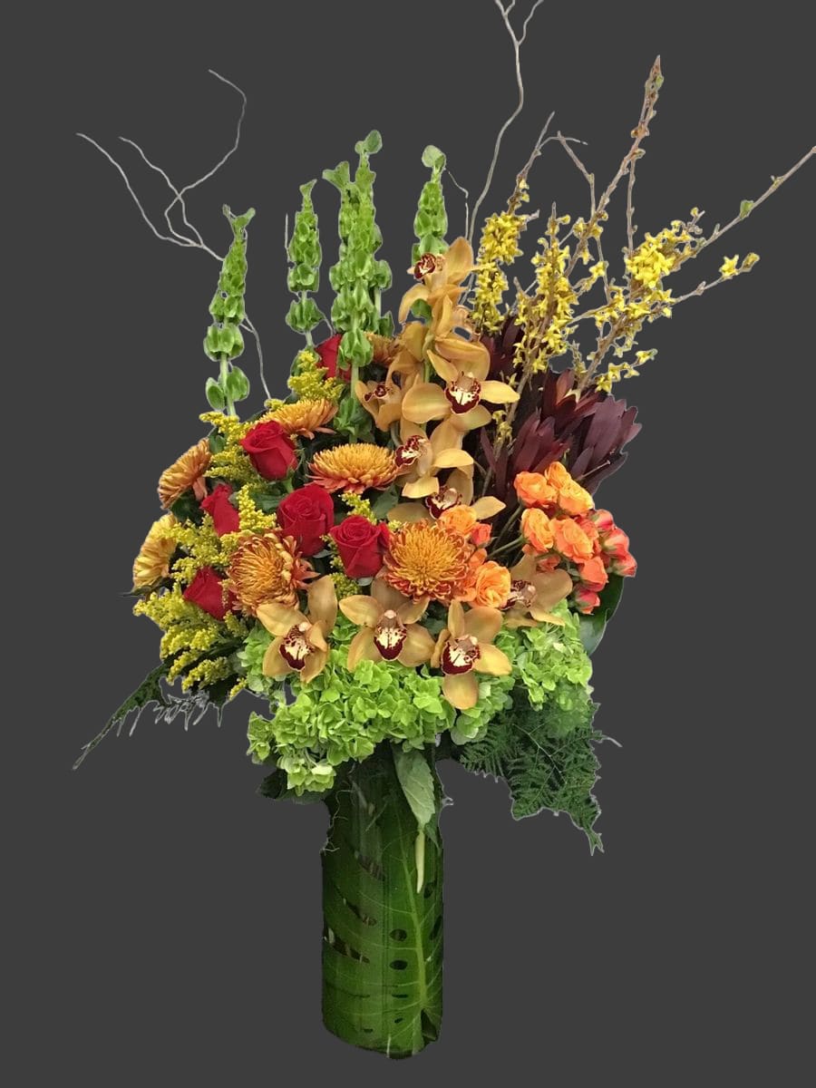 Tall mixed bouquet with red roses, orchids, and green hydrangeas in a wrapped vase
