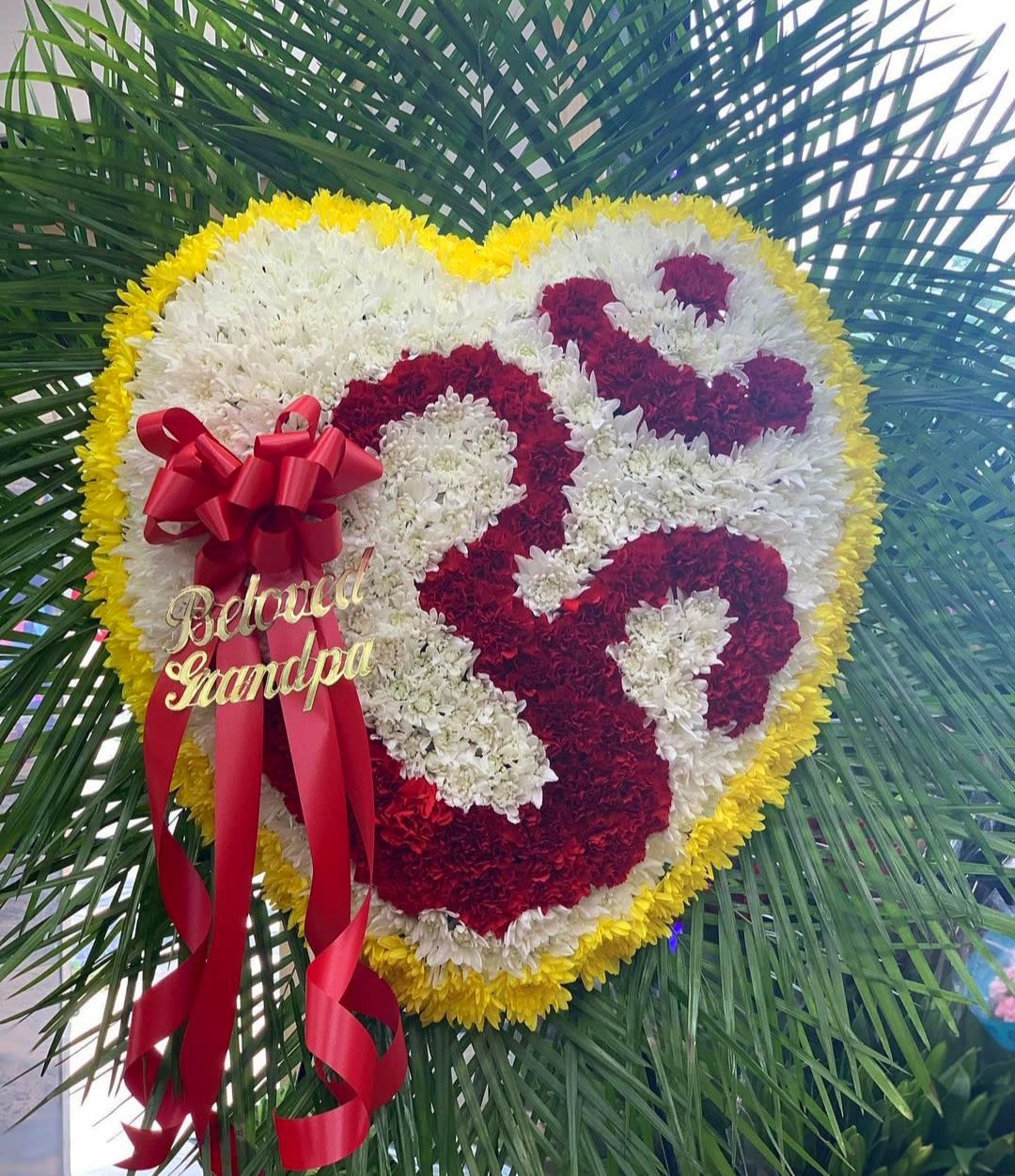 Heart-shaped floral tribute with red, white, and yellow flowers and a red ribbon