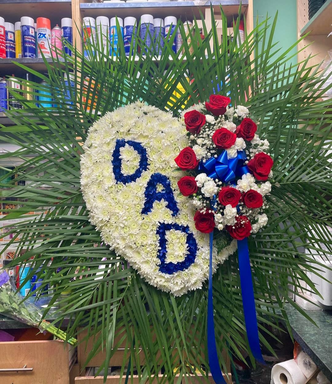 Heart-shaped floral tribute with white flowers, red roses, and blue letters