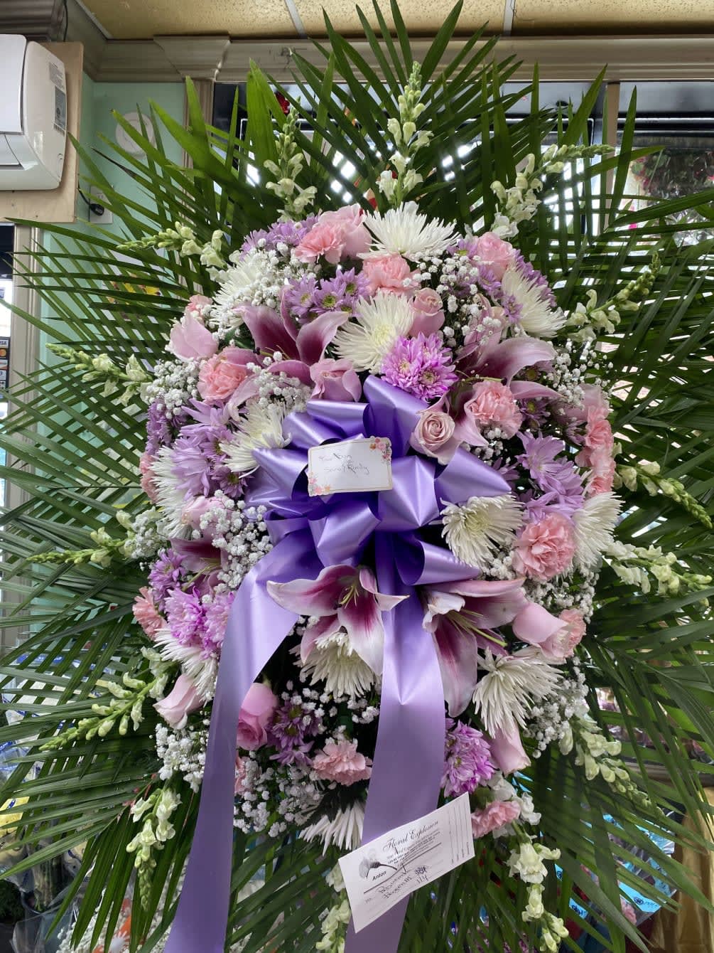 Large purple and pink funeral wreath with lilies and ribbon