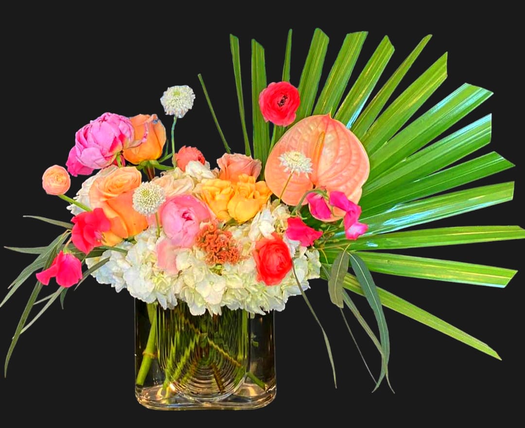 Colorful mixed bouquet in a clear glass vase with palm fronds