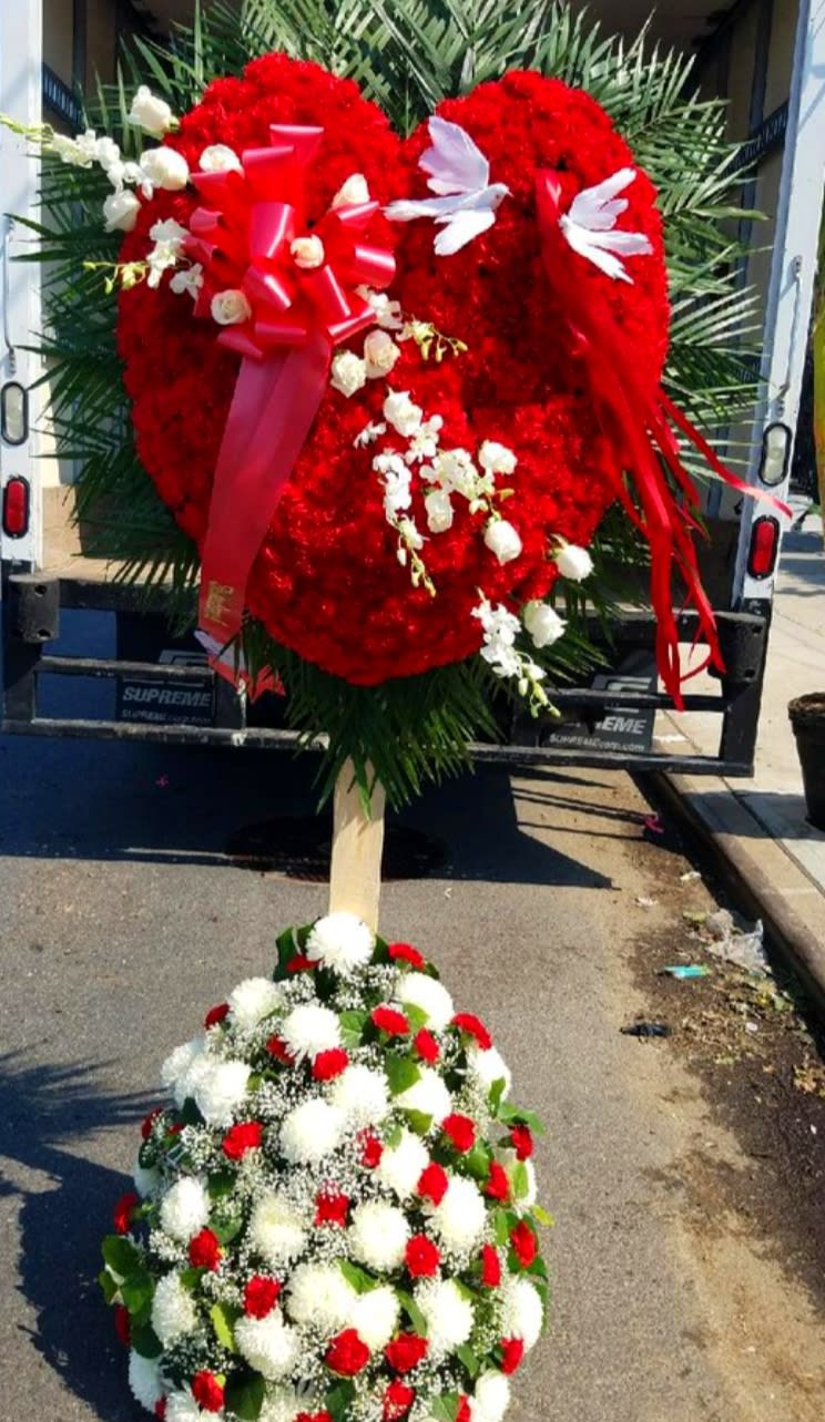Large red heart-shaped floral tribute with white accents on a stand