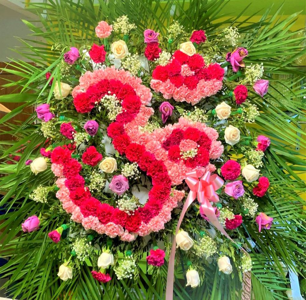 Heart-shaped floral wreath with pink and red flowers and a ribbon bow
