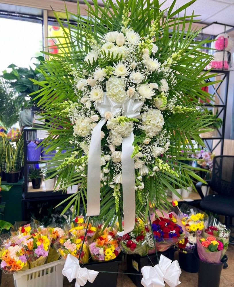Large white floral standing spray with palm fronds and a white ribbon