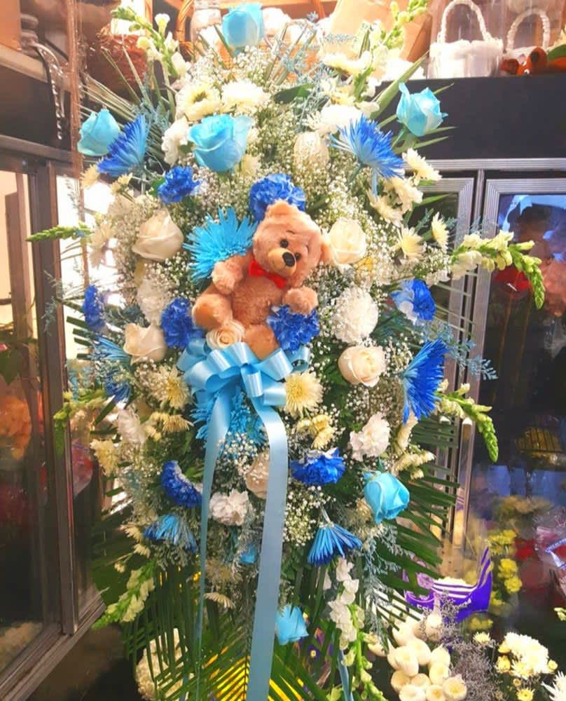 Tall floral standing spray with a teddy bear and blue ribbon